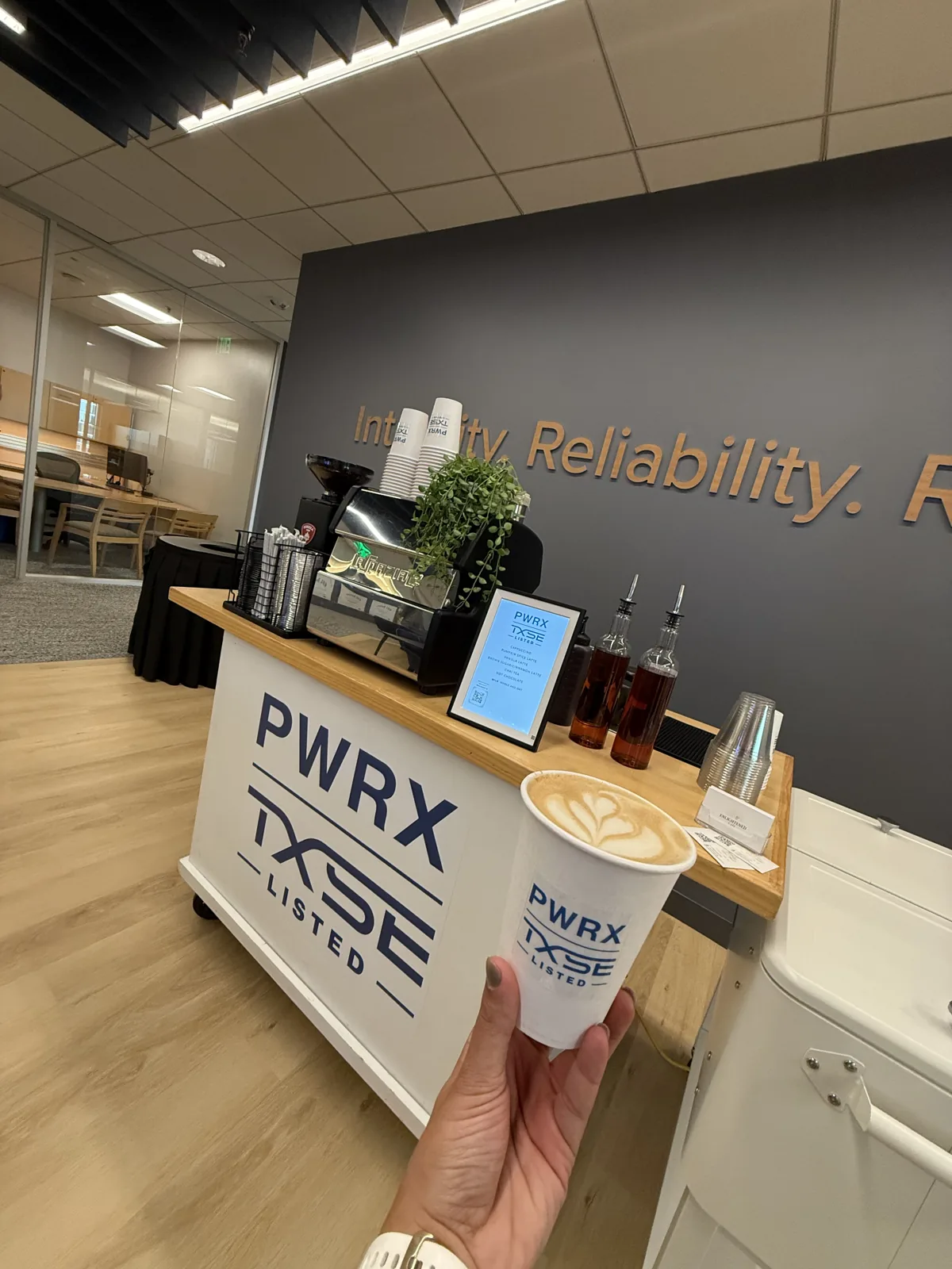 Latte art in a PWRX-branded cup in front of the matching logo-branded Enlightened Café coffee cart at a corporate office event
