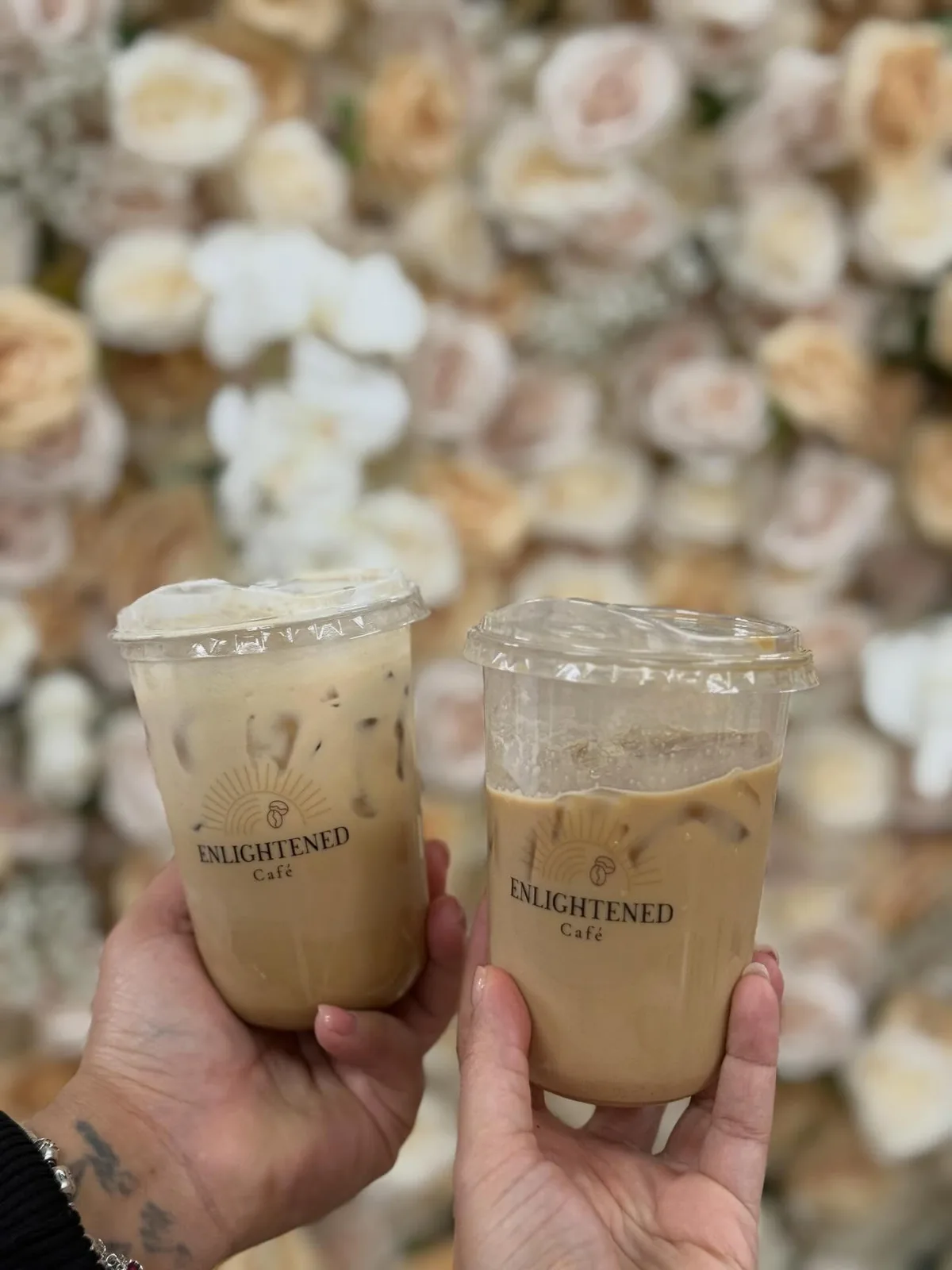 Two iced lattes in Enlightened Café branded cups in front of a wedding flower wall in Dallas–Fort Worth